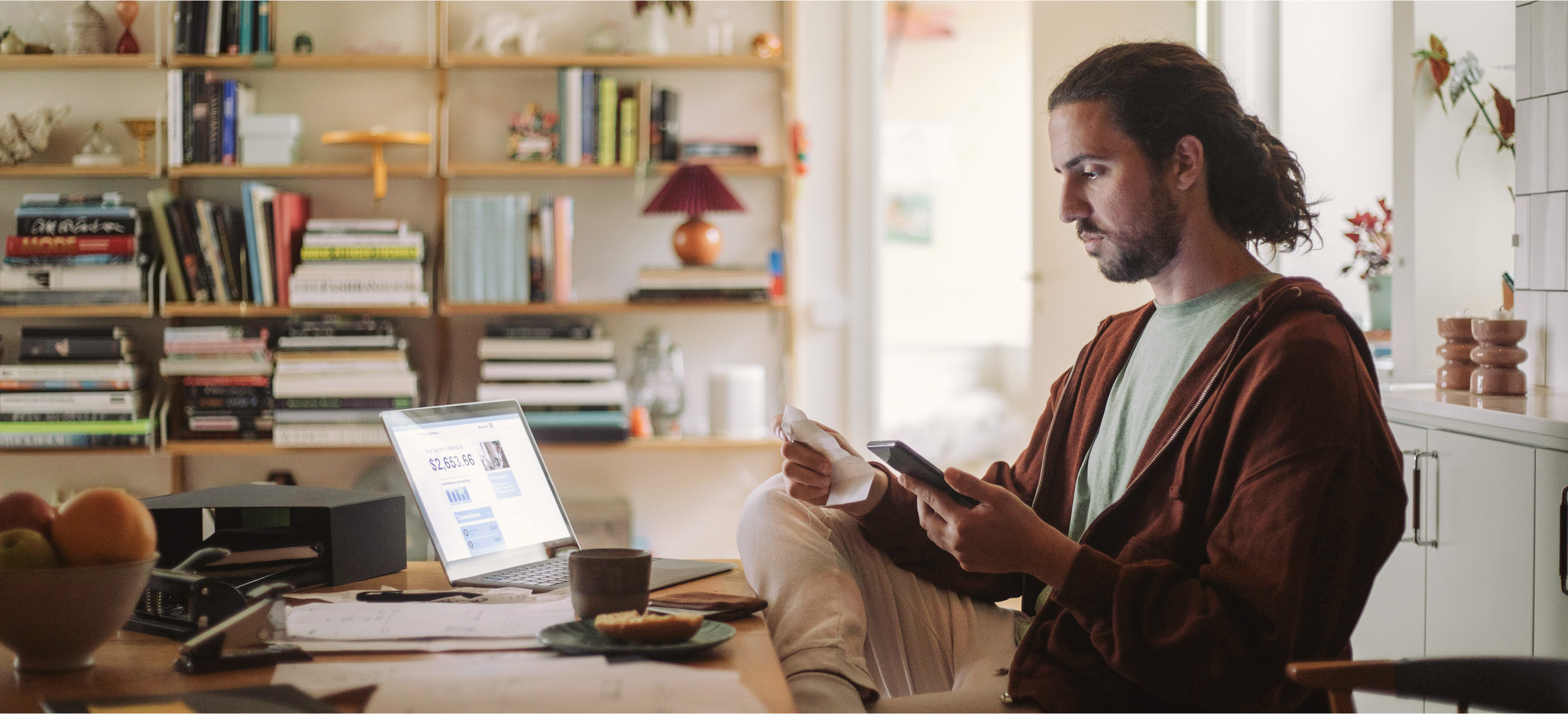 Man working at his desk looking at his phone and a receipt