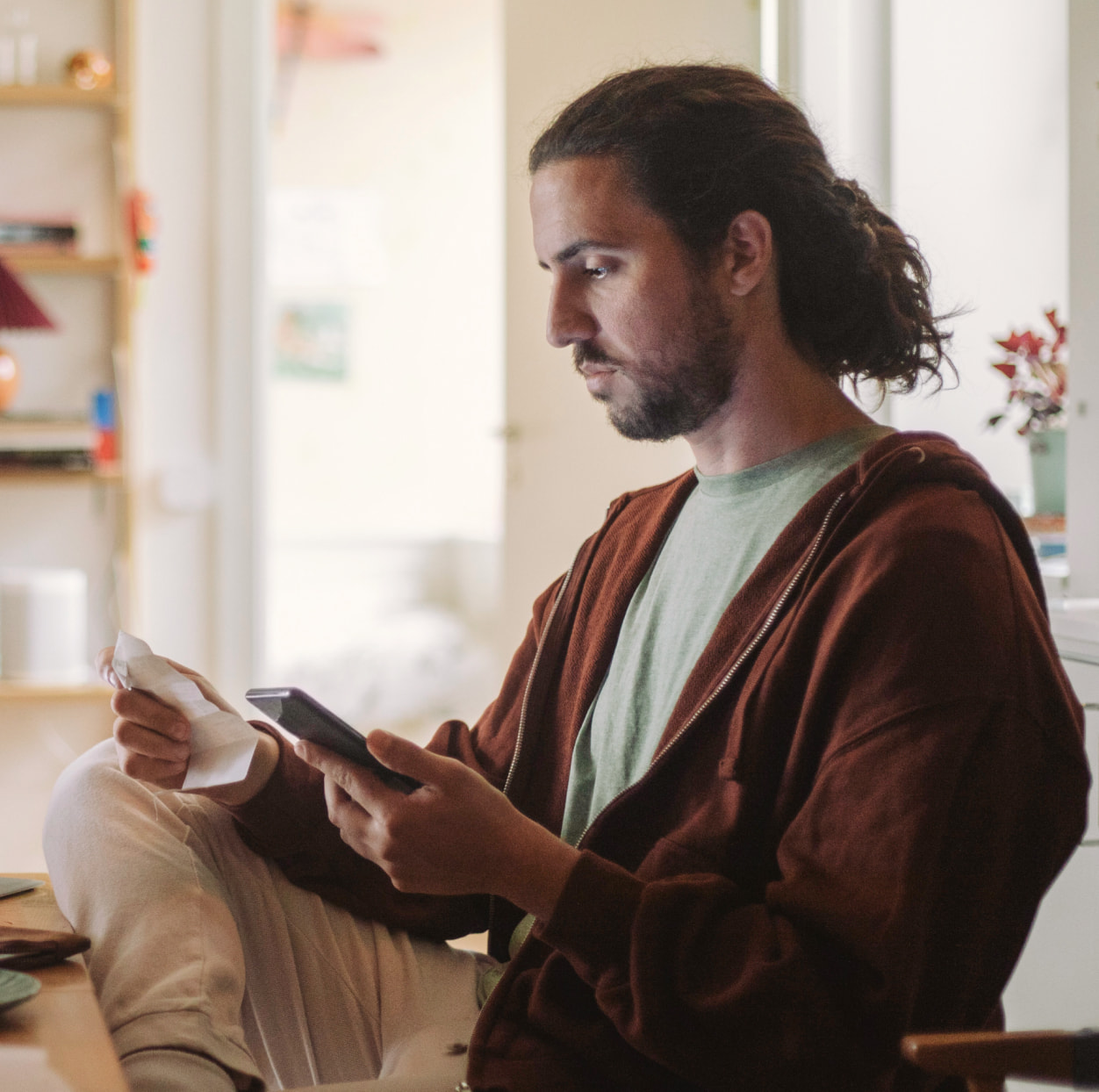 Man working at his desk looking at his phone and a receipt